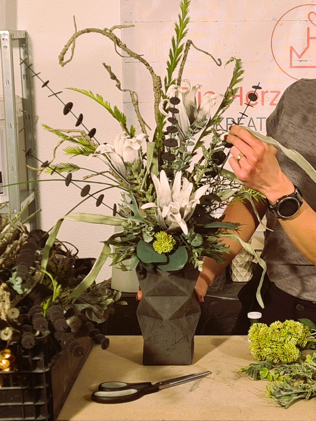 Inhaberin der Herzensdingfabrik arrangiert ein modernes Pflanzengesteck in ihre handgefertigte schwarze Blumenvase "Alex" aus Beton