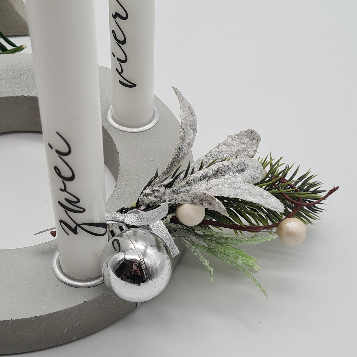 Detailansicht grauer Beton-Adventskranz „Concrete Circle“ mit winterlicher Dekoration und silberner Christbaumkugel, handgefertigt durch die Herzensdingfabrik