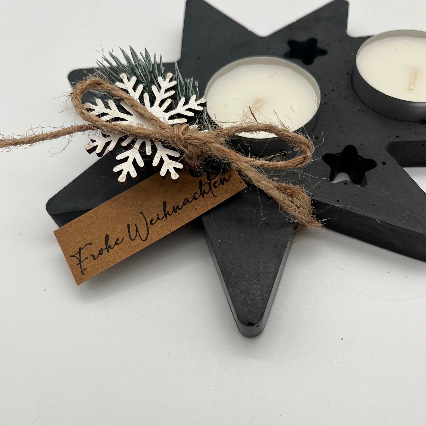 Detailaufnahme des schwarzen Beton-Teelichthalters Schweifstern mit weihnachtlicher Deko aus Tannenzweig, Schneeflocke und Frohe-Weihnachten-Label.
